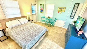 A bedroom with a bed, a desk, a chair, a small table with a plant, and a wall decoration.