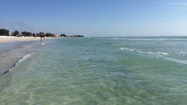 A beach with clear shallow waters and a sandy shore.