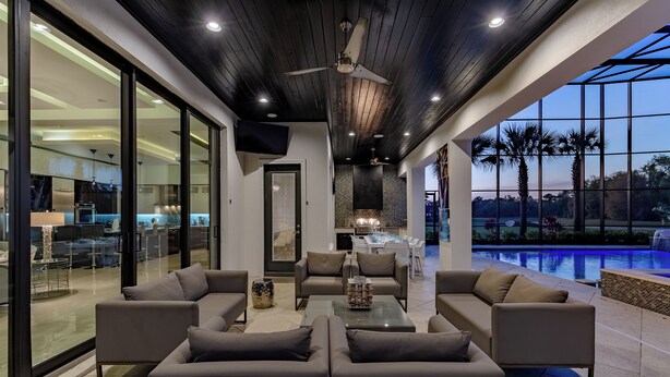 A modern living room with a pool view, large windows, and a ceiling fan. - Villatel Luxury Homes at Reunion Resort (Kissimmee)