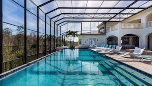 A swimming pool with a glass enclosure, lounge chairs, and a view of a building with balconies. - Villatel Luxury Homes at Reunion Resort (Kissimmee)