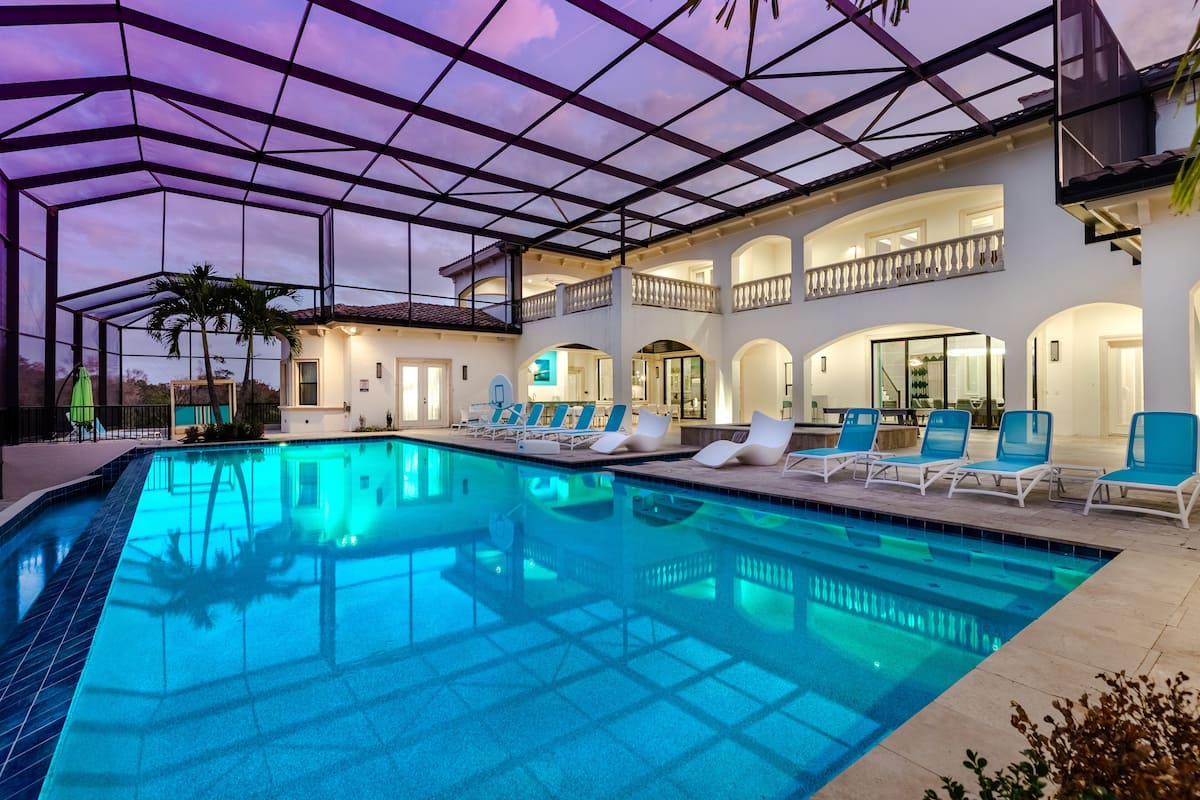 A swimming pool with lounge chairs, a covered patio, and a two-story building with balconies.