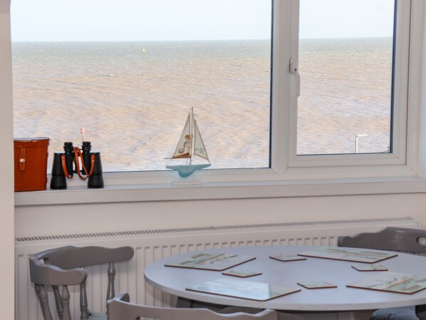 A room with a large window overlooking the sea, a table with papers, and a chair.