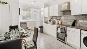 A modern kitchen with white cabinets, a built-in oven, microwave, and a stainless steel range hood. - Modern 4BR Victorian Home near Luton Airport (Luton)