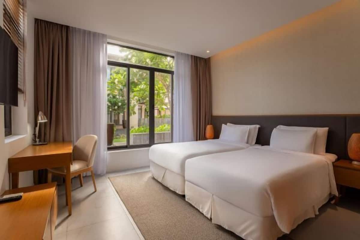 A hotel room with two beds, a desk, a chair, and a large window.