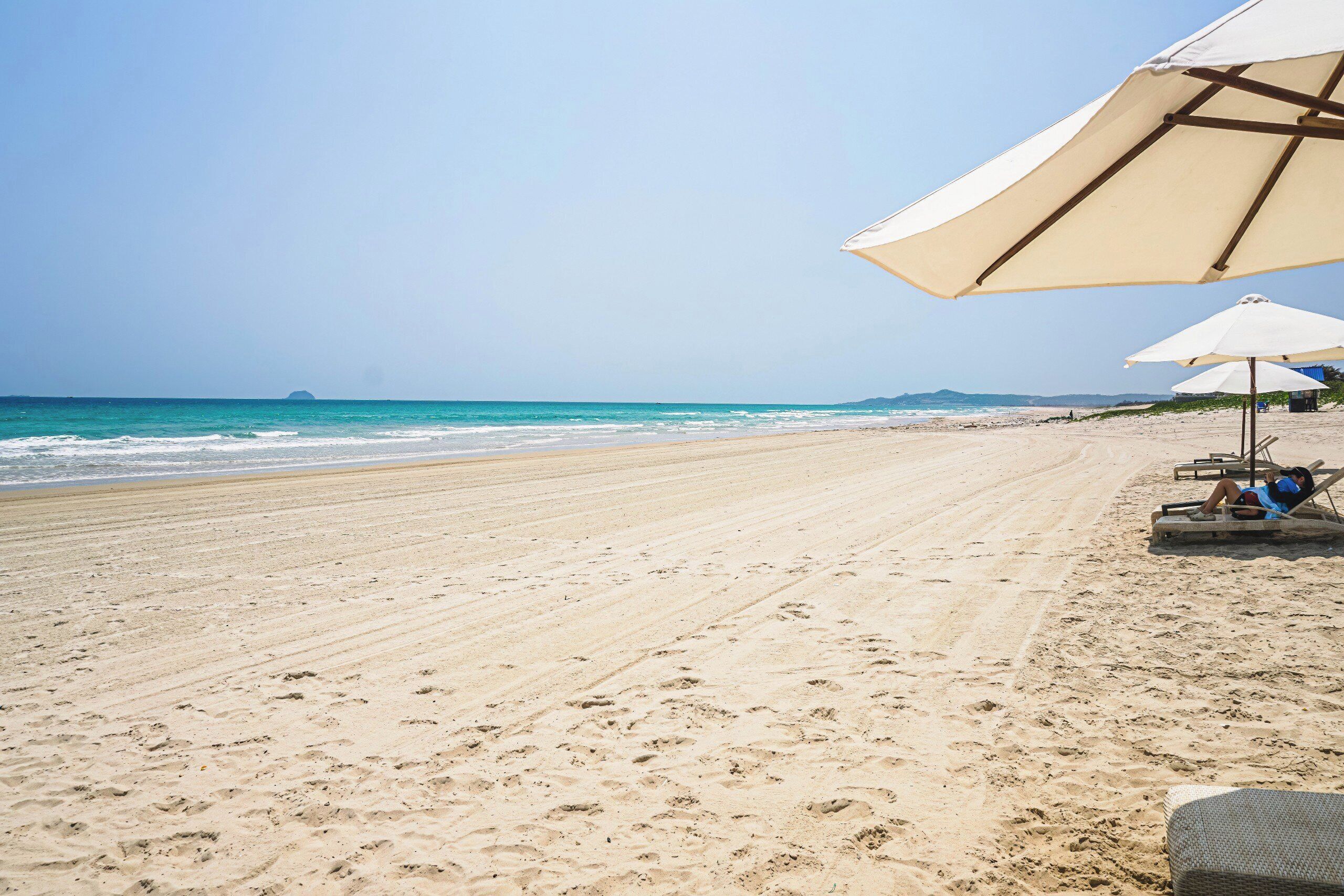 A beach with a clear sky, a sandy shore, and a few beach umbrellas.