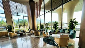 A spacious lobby with modern furnishings, large windows offering a view of palm trees, and a polished wooden floor. - Cam Ranh Mystery Villas & Resort (Cam Lam)