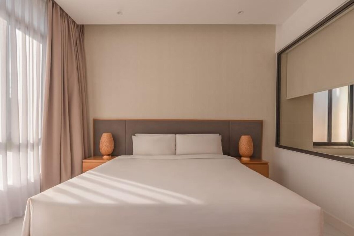 Ett modernt hotellrum med en stor säng, en sänggavel i trä, två sänglampor och en stor spegel på väggen.