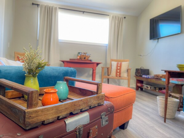 A cozy living room with a blue sofa, a wooden coffee table with a vintage suitcase, and a television on the wall. - The Fox Den, Pet Friendly, Broadband WiFi, Great Location (Ponca City)