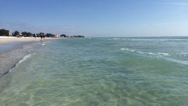 A beach with clear shallow waters and a sandy shore.