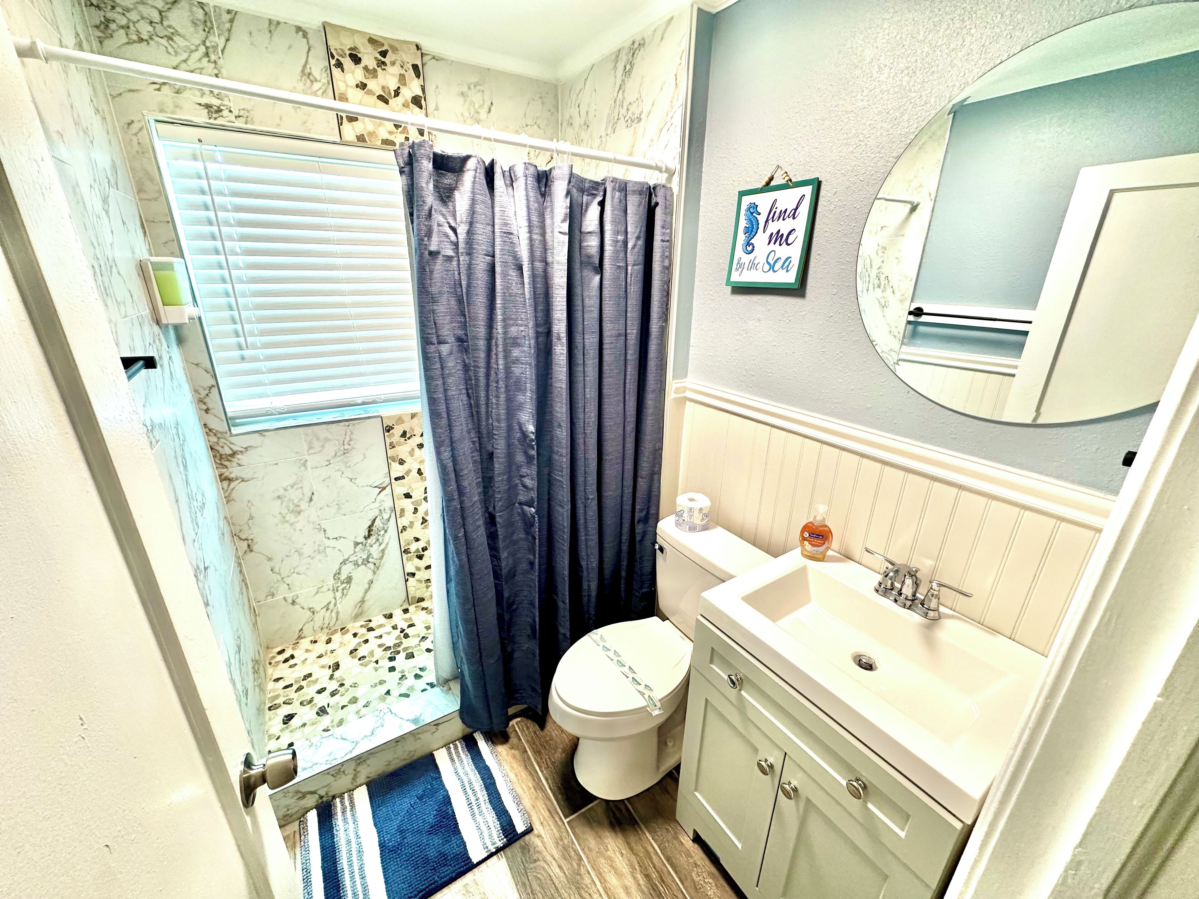 A bathroom with a shower, toilet, sink, and a mirror.