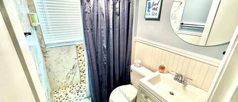 A bathroom with a shower, toilet, sink, and a mirror.