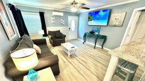 A living room with a sofa, a coffee table, a TV, and a dining area with a table and chairs.