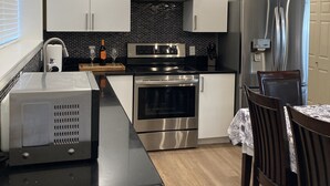 Una cocina moderna con armarios blancos, encimera negra, electrodomésticos de acero inoxidable y una zona de comedor con mesa y sillas.