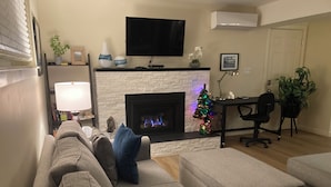 Una sala de estar con chimenea, televisor montado arriba, comedor con mesa y sillas, y un árbol de Navidad.