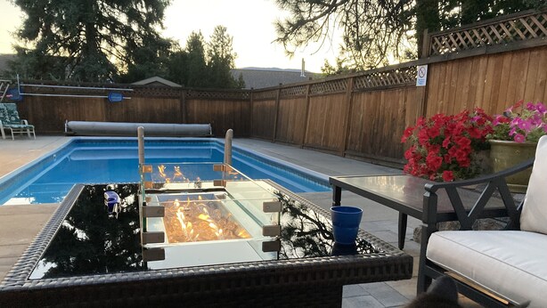 Un patio trasero con piscina, una mesa de vidrio y una silla.