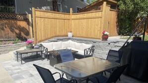 Un patio con un hogar a leña de piedra, una valla de madera y una zona de estar con mesa y sillas.
