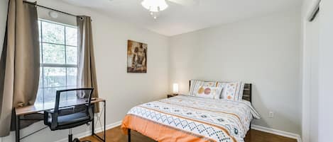 A bedroom with a bed, a desk with a chair, a ceiling fan, and a window with curtains.