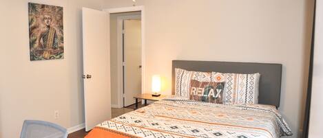 A bedroom with a bed, a desk, a chair, a ceiling fan, and a door.