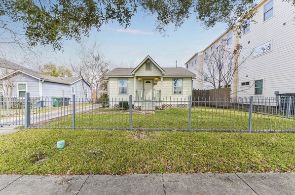 A residential house with a front yard, a metal fence, and a small tree.