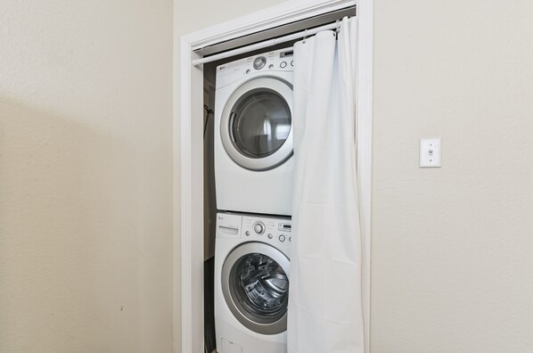 A laundry room with two stacked washing machines and a white curtain.