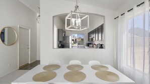 Uma área de jantar moderna com uma mesa branca, seis cadeiras e um lustre central.