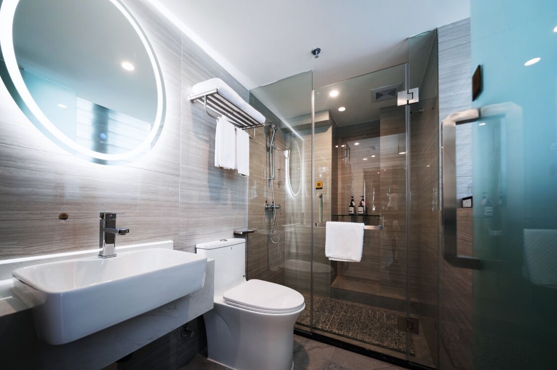 Een moderne badkamer met een douchecabine van glas, een ronde spiegel en een witte wastafel.