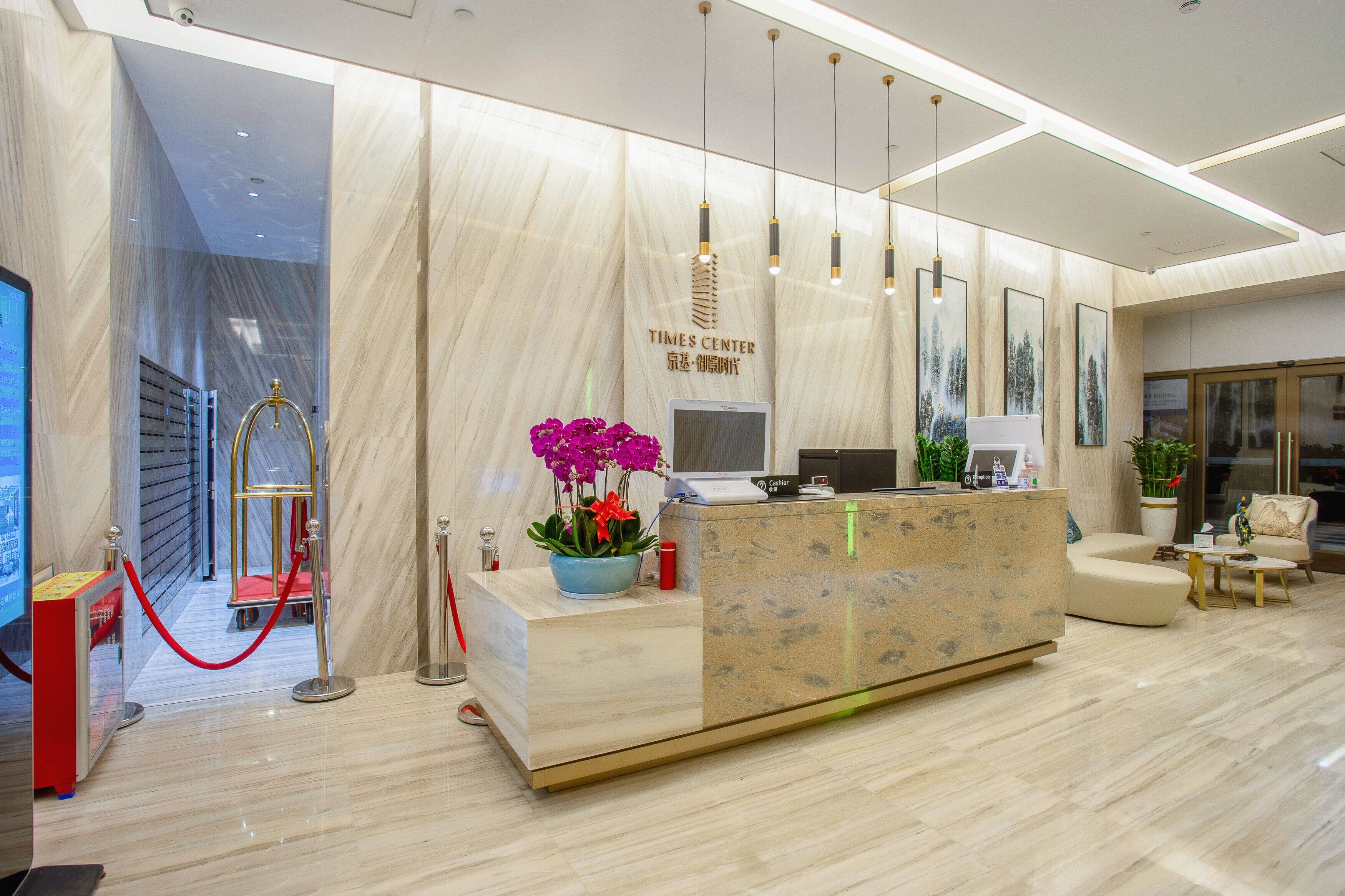 A modern reception area with a marble reception desk, a red velvet rope barrier, and a seating area with a sofa and armchairs.