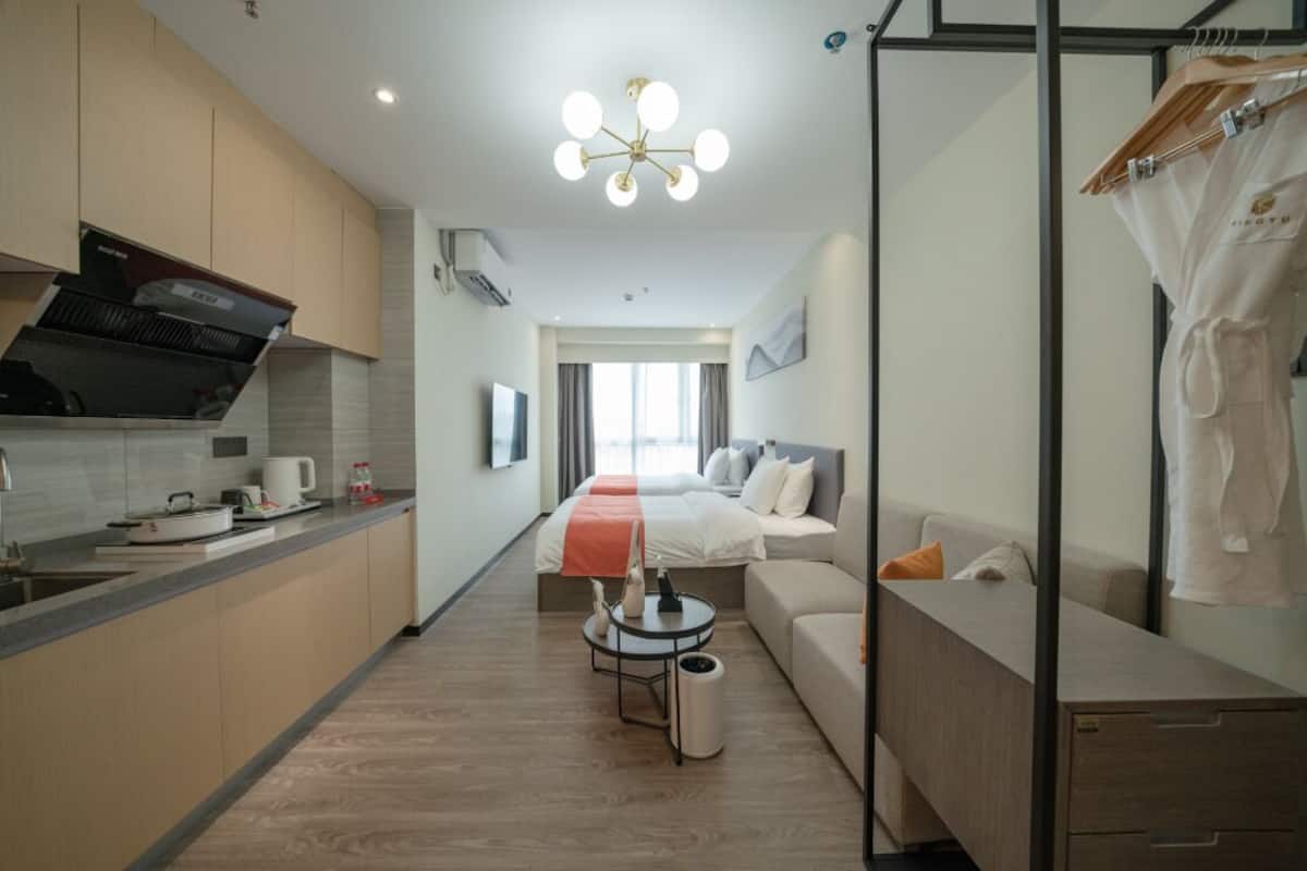 Una habitación de hotel moderna con kitchenette, una cama con manta roja, un sofá y un escritorio.