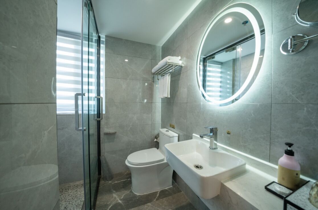 A modern bathroom with a glass shower enclosure, a toilet, a sink, and a mirror with a circular light.