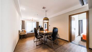A hotel room with a wooden floor, a dining table with chairs, a large mirror, and a bed with an orange blanket.