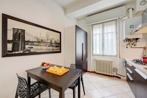 Et spiseområde med et bord, stole, en frugtfat og et indrammet bybillede.