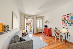 En moderne stue med en sofa, et skrivebord, en stol og udsigt gennem en åben dør.
