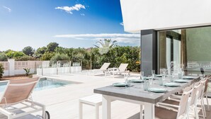 Ein moderner Essbereich im Freien mit Pool, heller Möbel und freiem Blick zum Himmel.
