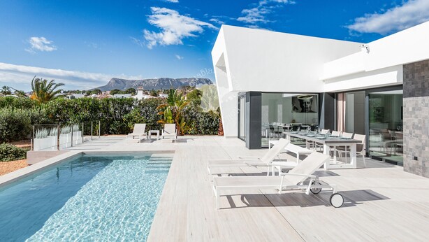 Ein moderner Poolbereich im Freien mit Liegestühlen und Essbereich, mit Blick auf eine Berglandschaft.