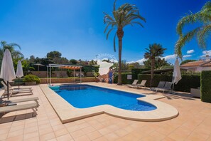 Une piscine à bord incurvé, entourée de chaises longues et de parasols, avec des palmiers et un ciel dégagé en arrière-plan.
