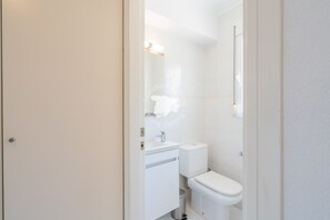Une petite salle de bain blanche, avec des toilettes, un lavabo et un miroir.
