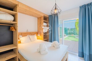Ein Schlafzimmer mit einem hölzernen Kopfteil, einem Bett mit weißer Bettwäsche, einer Pendelleuchte und Blick auf einen Garten durch eine Glastür.