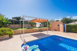 Ein Swimmingpool mit weißem Pergola und Sonnenschirm, umgeben von einer Steinmauer und Pflanzen.