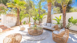 Eine Terrassengruppe im Freien mit Korbmöbeln, einem runden Glastisch und einem weißen Sofa.