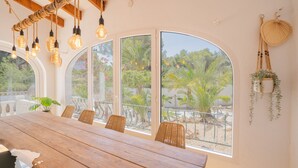 Ein Essbereich mit Holztisch, Korbstühlen und großen Rundbogenfenstern mit Blick auf einen Garten.