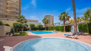 A swimming pool with lounge chairs, palm trees, and a high-rise building in the background. - CostaBlancaDreams - Maroen in Calpe (Calpe / Calp)