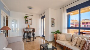 A living room with a sofa, a coffee table, a dining area with chairs and a table, and large windows with a view of buildings. - CostaBlancaDreams - Maroen in Calpe (Calpe / Calp)