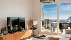 Un salon moderne doté d’un grand téléviseur à écran plat, d’une console en bois, d’un canapé et d’un coin repas avec une table ronde et des chaises.