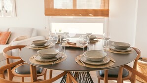 Une table à manger dressée avec des bols, des verres et des couverts, entourée de chaises en bois dotées de coussins.