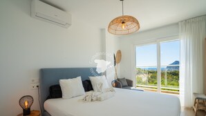 Une chambre avec un grand lit, une vue sur la mer et une lampe en osier.