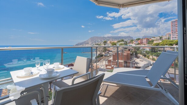 Een balkon met een eettafel, met uitzicht op een kustplaats met gebouwen en een berg in de verte.