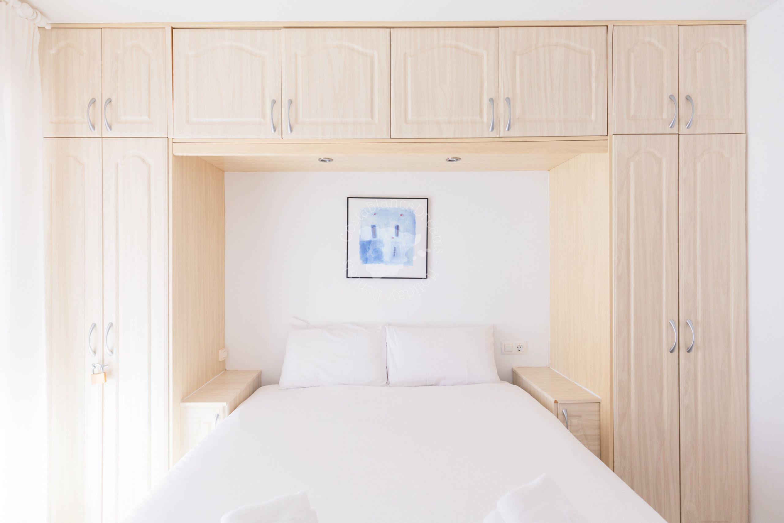 A bedroom with a bed, wooden wardrobe, and a framed picture on the wall.