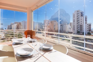 A dining table set with plates, glasses, and cutlery in a room with large windows overlooking a cityscape.