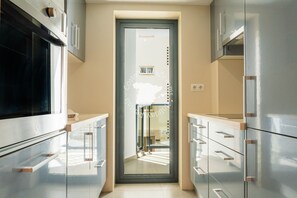 Une cuisine moderne dotée d’appareils électroménagers en acier inoxydable, une porte en verre donnant sur un coin repas et une vue sur la rue.