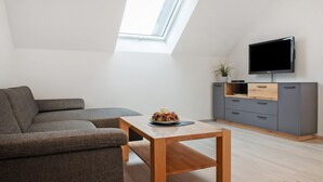 A modern living room with a sofa, a wooden coffee table, a TV on a stand, and a skylight.